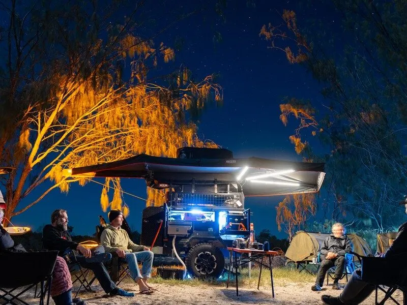 Campers at night under a 4WD awning lit by 12V camp lights