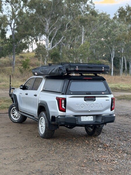 Rear view of a Toyota HiLux N90 with a canopy and rooftop tent on a gravel track