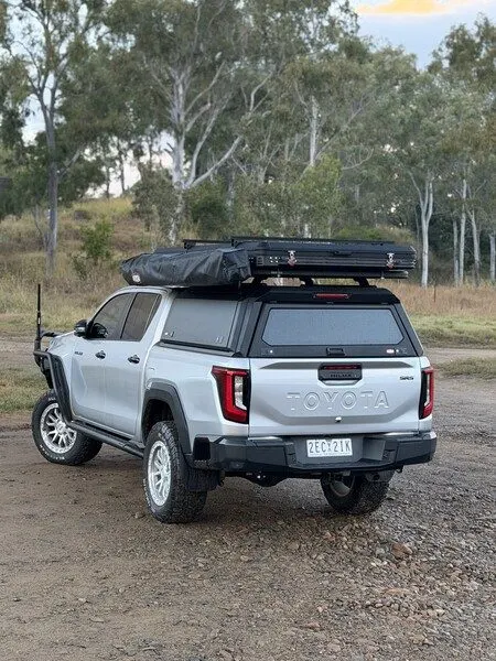 Rear view of a Toyota HiLux N90 with a canopy and rooftop tent on a gravel track