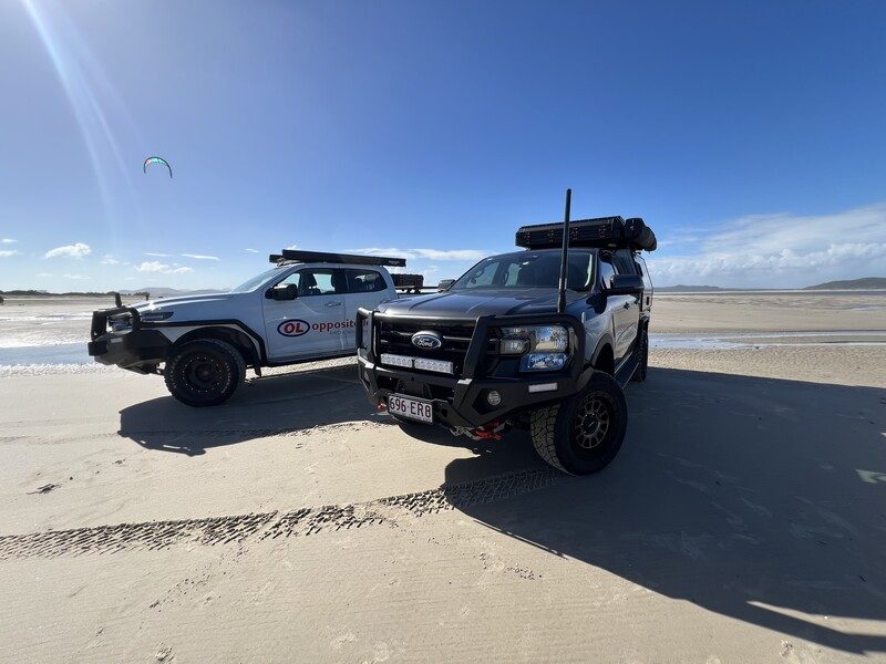 Two Ford Rangers fitted with Opposite Lock bull bars and roof racks on a beach